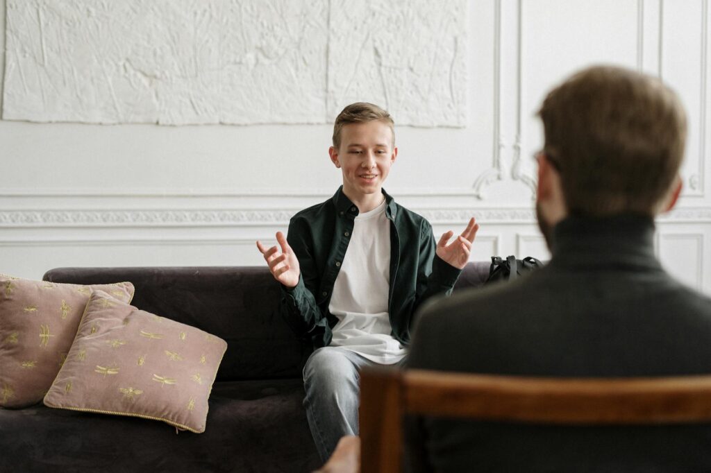 man in black suit jacket sitting on brown wooden chair